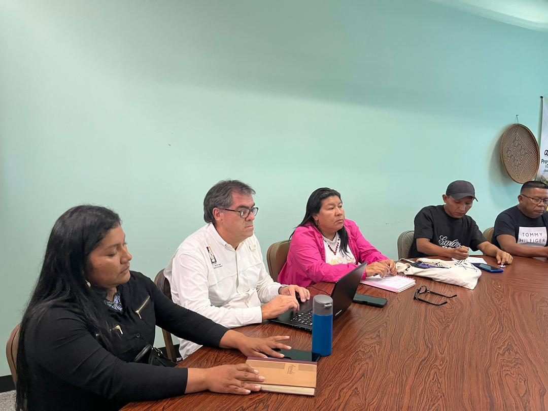 Vladimir Aguilar Castro, con camisa blanca, trabajando en su ordenador durante una sesión de trabajo junto a representantes indígenas