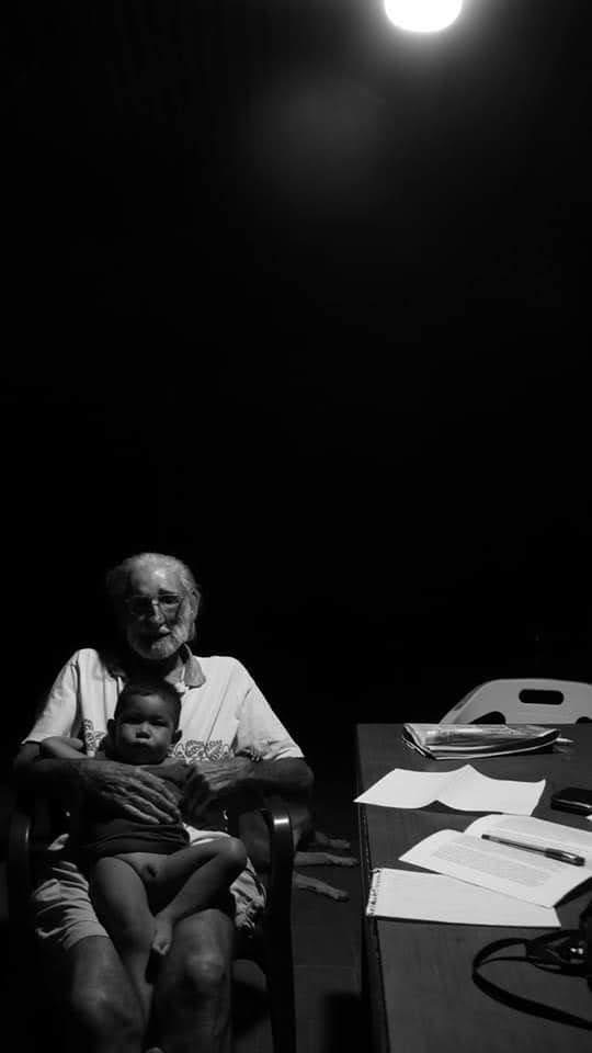 Retrato histórico en blanco y negro del padre José María Korta sosteniendo a un niño indígena en un espacio comunitario, bajo la luz de una bombilla